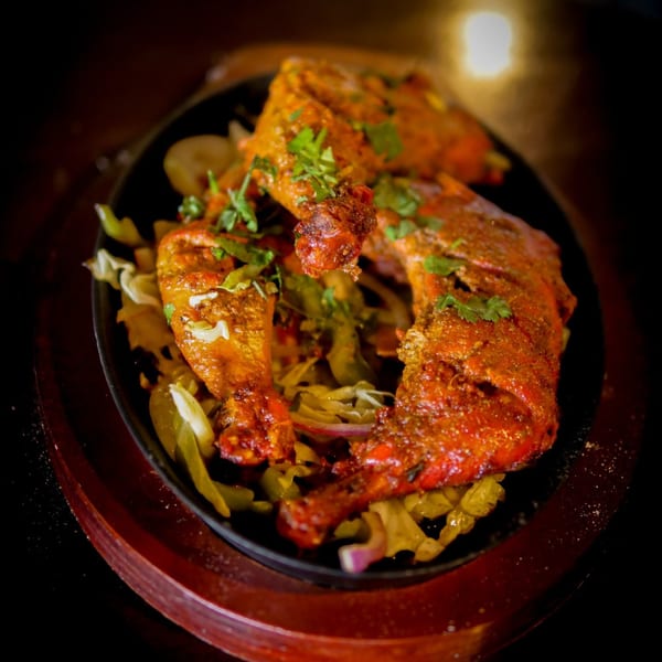 Indian tandoori chicken legs garnished with cilantro and served on a bed of cabbage.