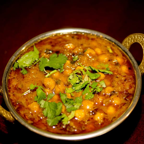 Close-up of Indian chana masala curry with chickpeas and cilantro in a metal bowl.