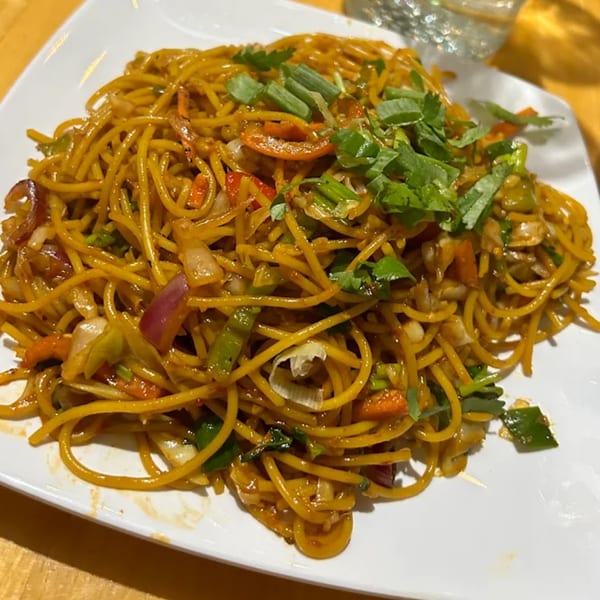 A plate of Indian noodles with vegetables, garnished with fresh green herbs.