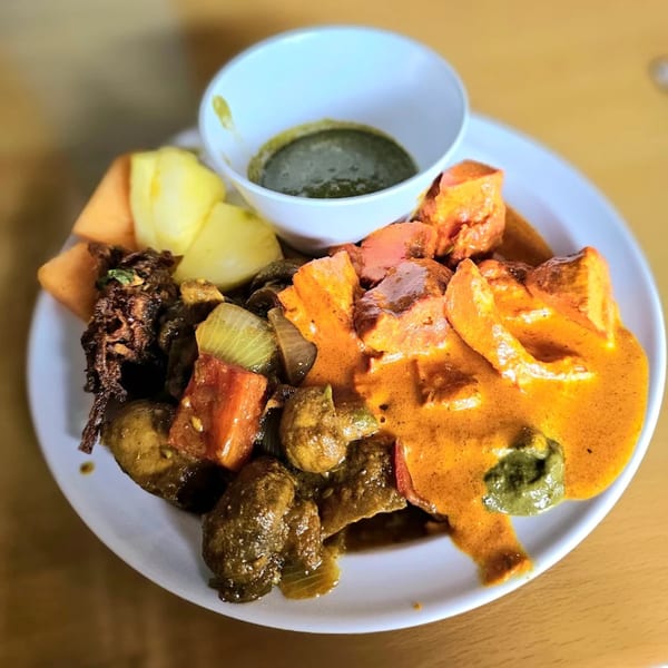 A vibrant Indian dish with orange curry, green sauce, and various vegetables on a white plate.
