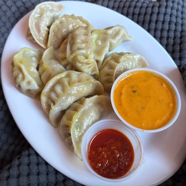A plate of steamed momos with two dipping sauces, one orange and one red, from Namaste Momo.