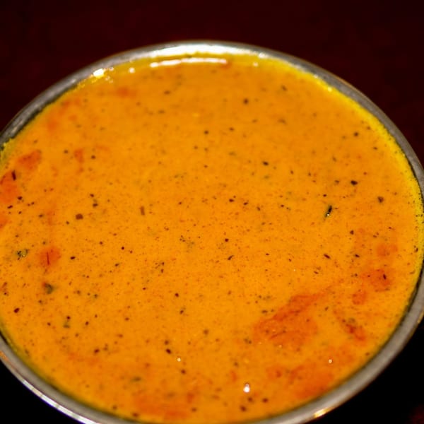 Close-up of a vibrant orange Indian curry or sauce with specks of spices in a metal bowl.