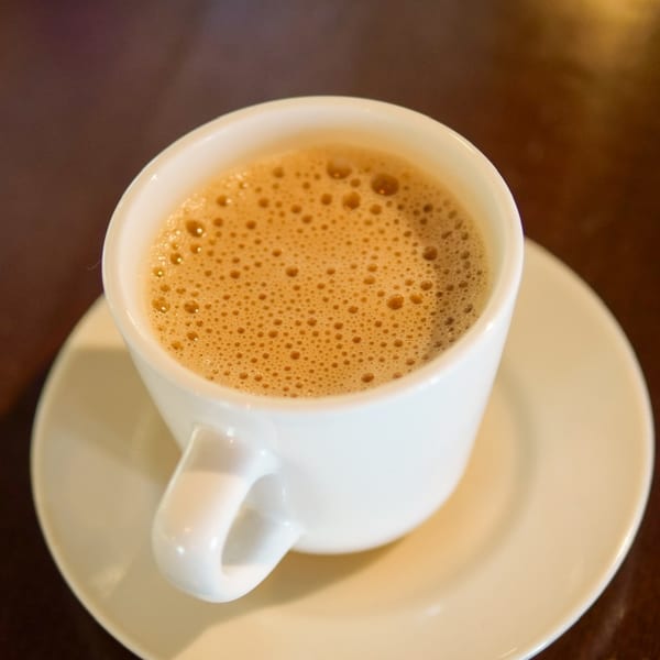 A white cup of frothy, light brown Indian chai tea on a matching saucer.